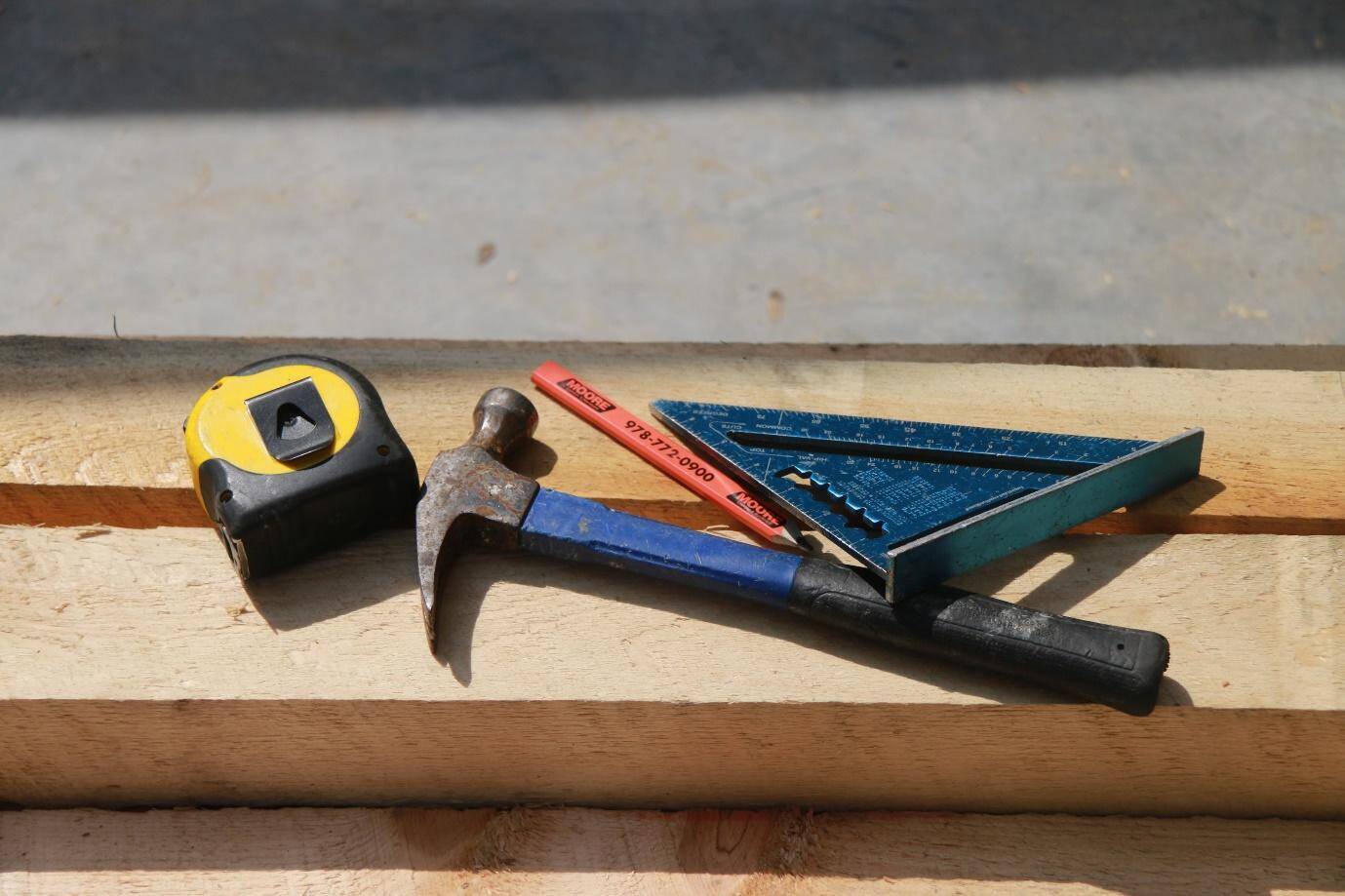 a tape measure, hammer, pencil, and angle finding protractor on top of a plank of wood