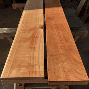 Stacked cherry wood boards glowing in sunlight on a workbench, showing smooth grain and deep reddish color.”
