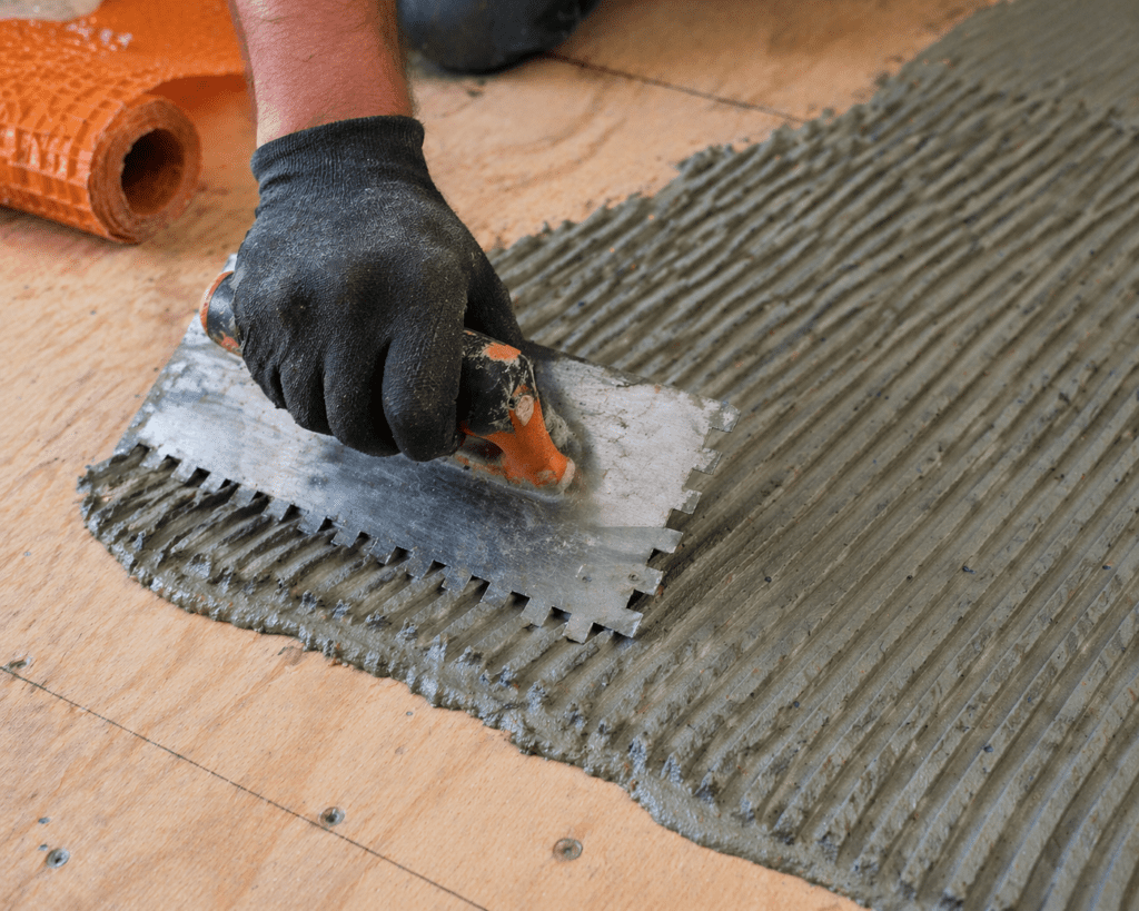 Applying thinset mortar with square notch trowel on plywood subfloor