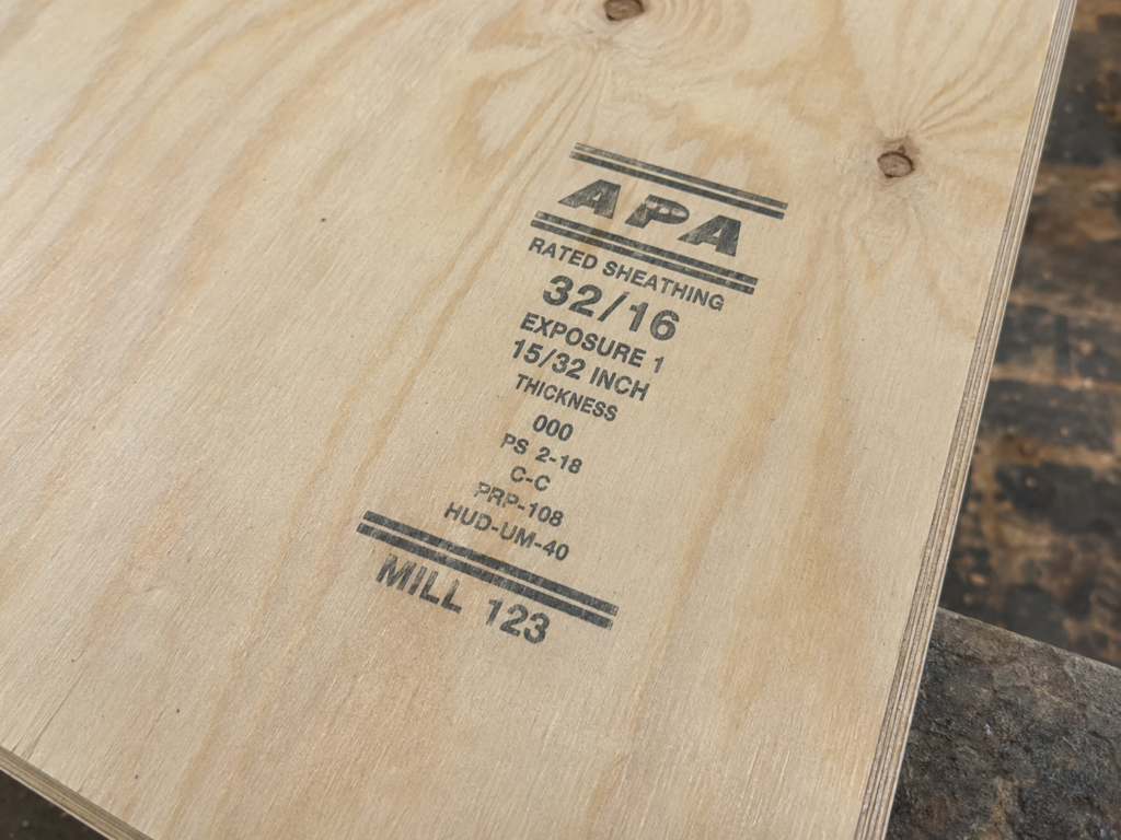 Close-up of a plywood grade stamp showing Rated Sheathing, 32/16 span rating, Exposure 1, thickness, mill number, and PS 2-18 standard.